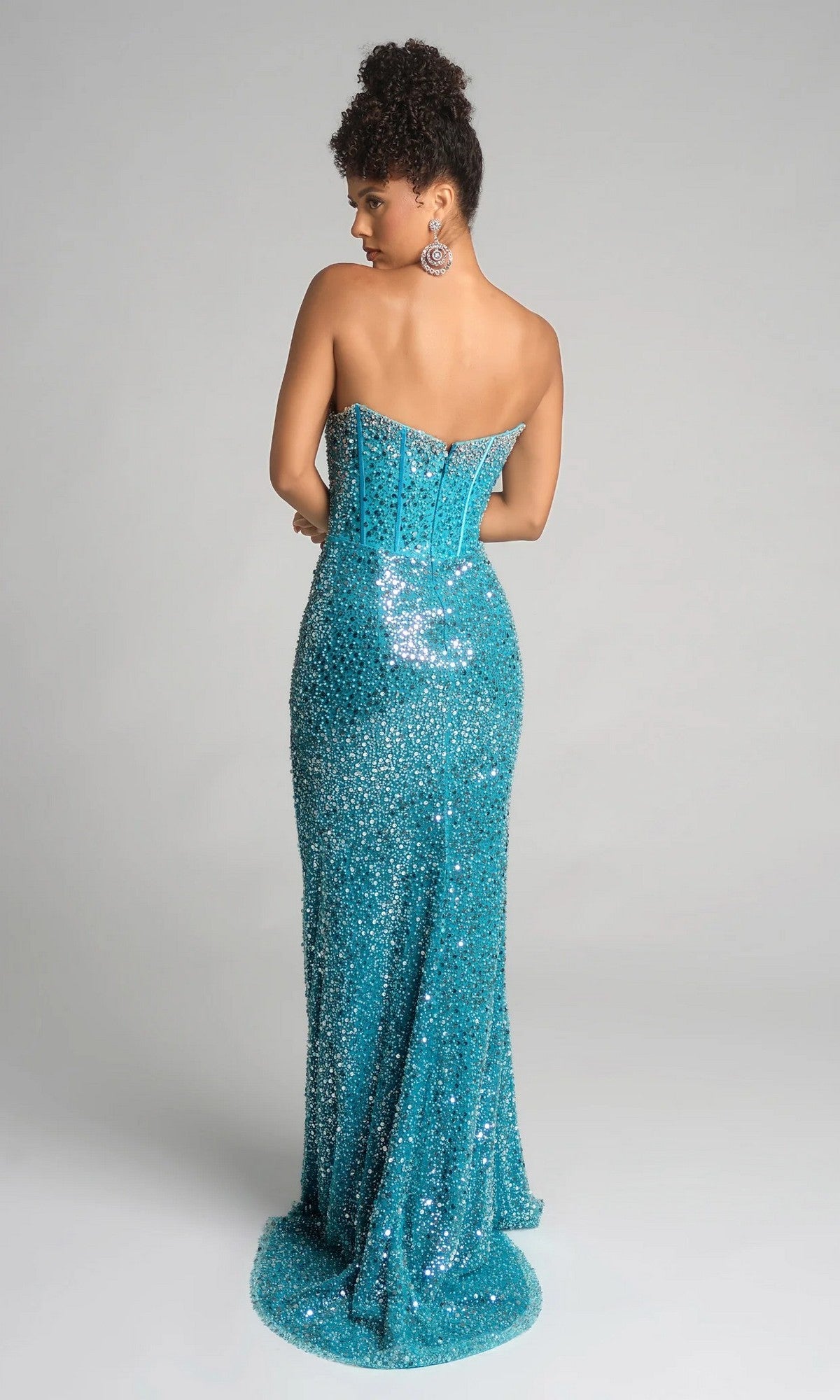 A woman stands with her back to the camera, wearing the Portia and Scarlett XO054: a strapless, turquoise sequin long formal dress with a fitted corset bodice and flared floor-length hem.